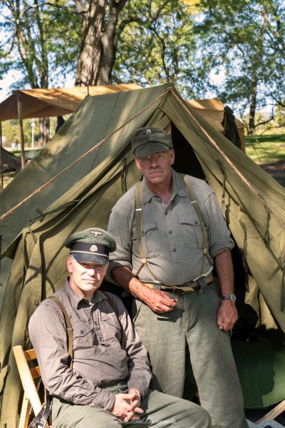 "Group portrait of German soldiers at Lauer Farms, showcasing their distinctive World War II uniforms and equipment. The soldiers stand together with serious expressions, embodying the complexities of war. The rustic backdrop of the farm contrasts with the military presence, highlighting the juxtaposition of daily life and the realities of conflict. Details such as insignia and gear reflect their military identity. Soft natural light enhances the scene, creating a dramatic yet respectful atmosphere."